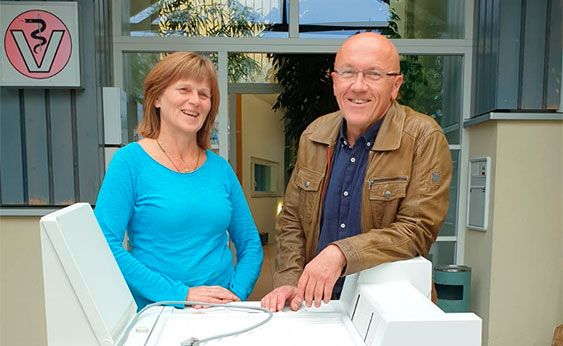 Zwei Mitarbeitende des Tierärzte Teams Tiefenbach stehen vor der Praxis und präsentieren ein medizinisches Gerät